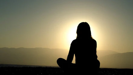 Woman sitting outdoors in soft natural light, reflecting calmly and beginning to let go of emotional weight